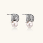 Curved pavé diamond studs in white gold-plated brass cradle lustrous freshwater pearls against cream background