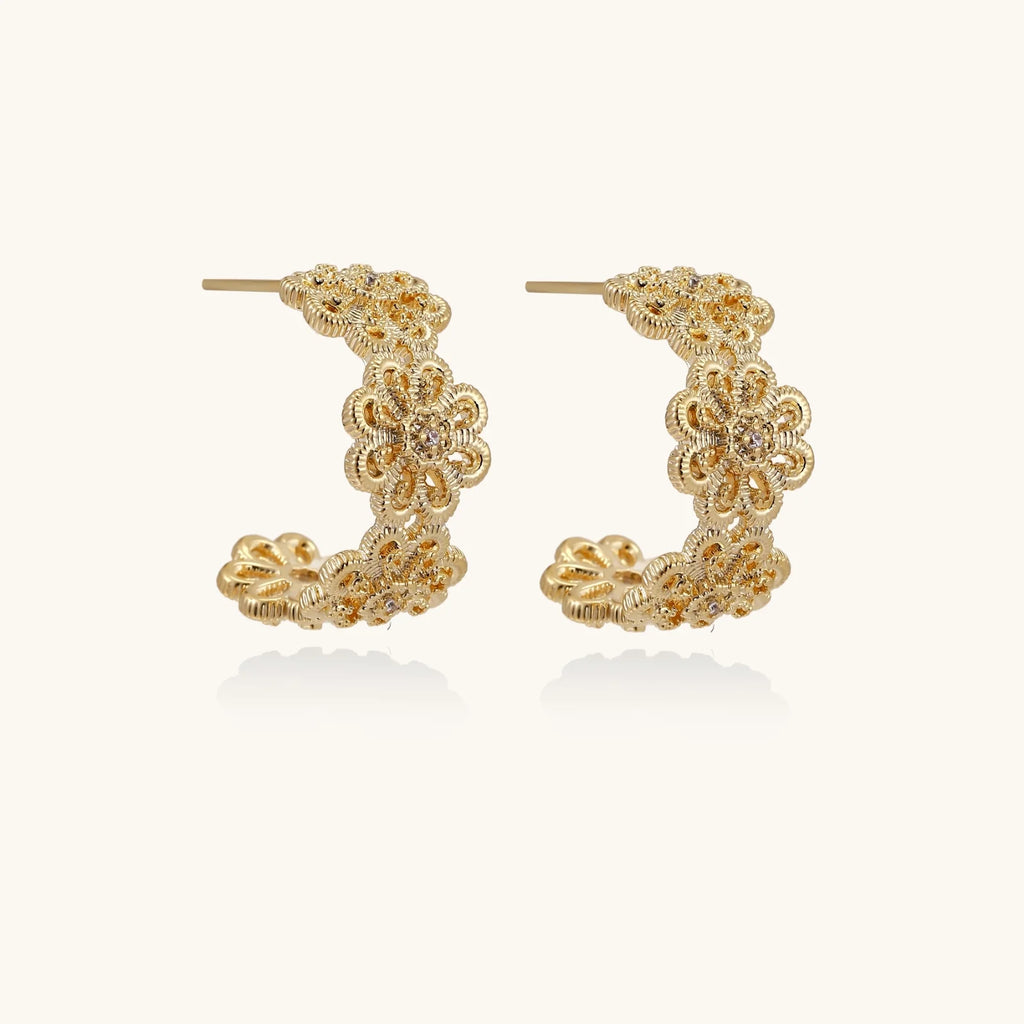 Gold hoop earrings with intricate three-dimensional floral filigree pattern in 14K gold plated brass on cream background