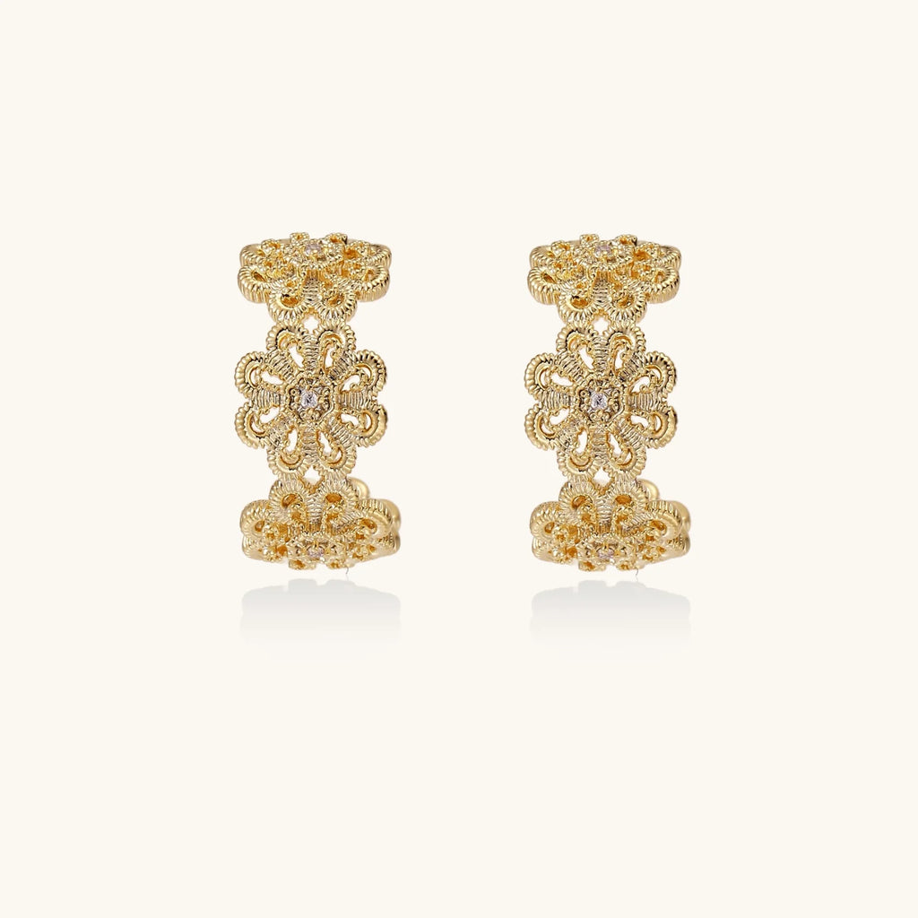 Gold hoop earrings with intricate three-dimensional floral filigree pattern in 14K gold plated brass on cream background