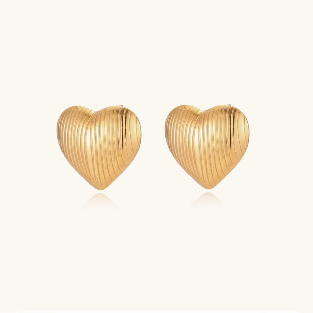 Gold heart-shaped stud earrings with parallel ridged texture on cream background