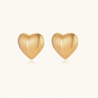 Gold heart-shaped stud earrings with parallel ridged texture on cream background