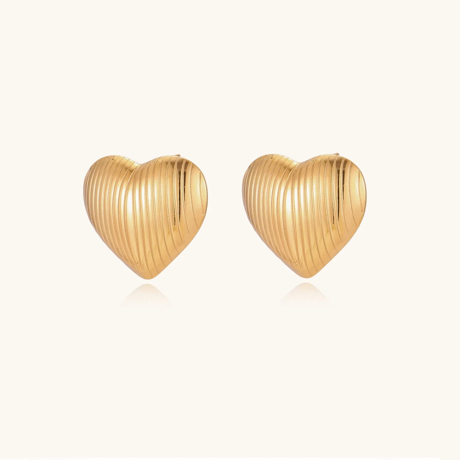 Gold heart-shaped stud earrings with parallel ridged texture on cream background