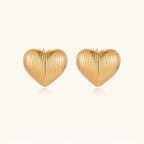 Gold heart-shaped stud earrings with parallel ridged texture on cream background