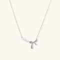 Delicate white gold plated necklace with graduated freshwater pearls and crystal-studded bow pendant on ivory background