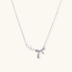 Delicate white gold plated necklace with graduated freshwater pearls and crystal-studded bow pendant on ivory background