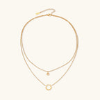 Gold layered necklace set with sunburst and smiley face pendants on delicate chains against white background.