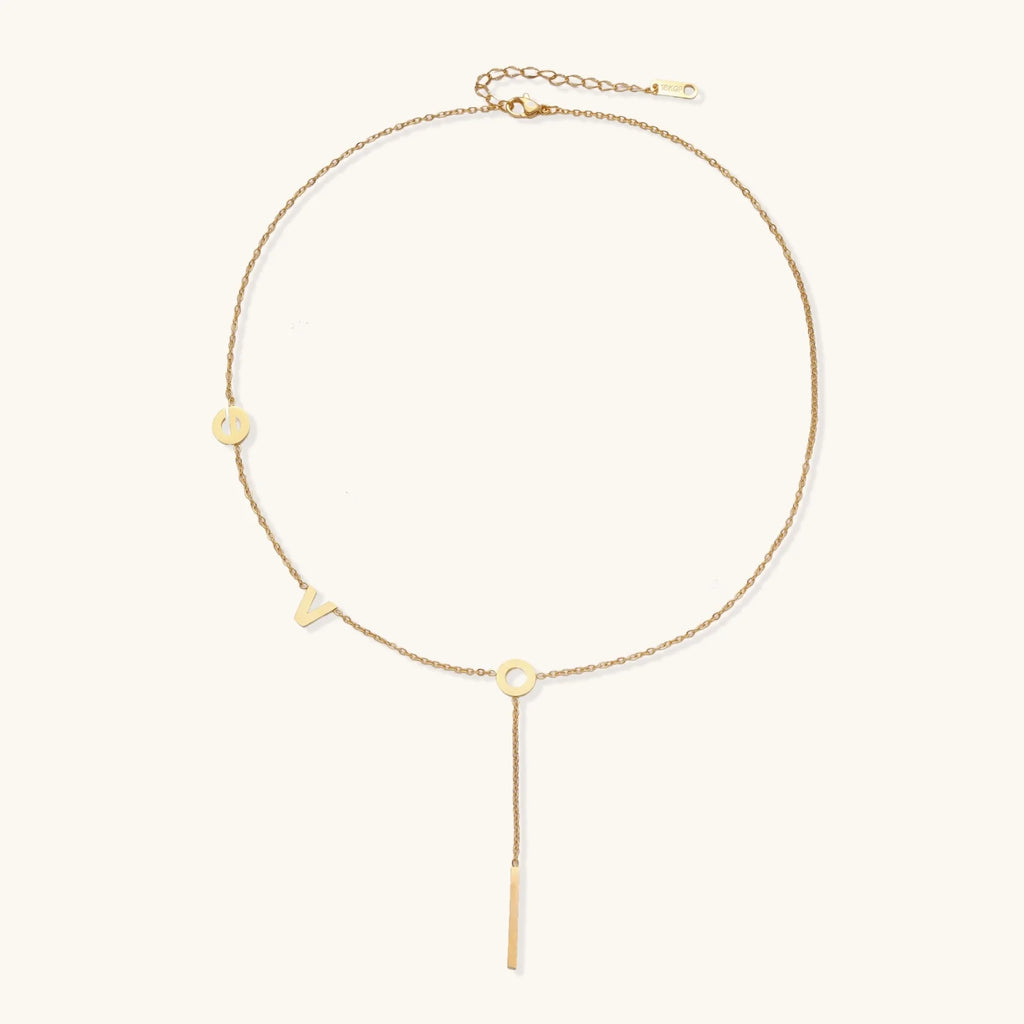 Gold Y-shaped necklace with L-O-V-E letter charms and vertical bar pendant on delicate chain against cream background