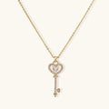 Delicate gold key pendant with heart-shaped bow and crystal pavé detailing on fine chain against cream background.