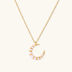 Gold crescent moon pendant with graduated white pearls on delicate chain against cream background