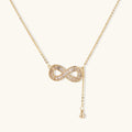 Gold infinity pendant with baguette crystals on adjustable chain against cream background.