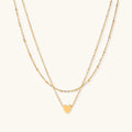 Delicate double-chain gold necklace with tiny heart pendant on cream background