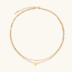 Delicate double-chain gold necklace with tiny heart pendant on cream background