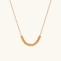 Delicate gold-plated necklace with graduated spherical beads forming gentle smile curve on beige background