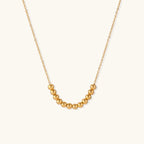 Delicate gold-plated necklace with graduated spherical beads forming gentle smile curve on beige background