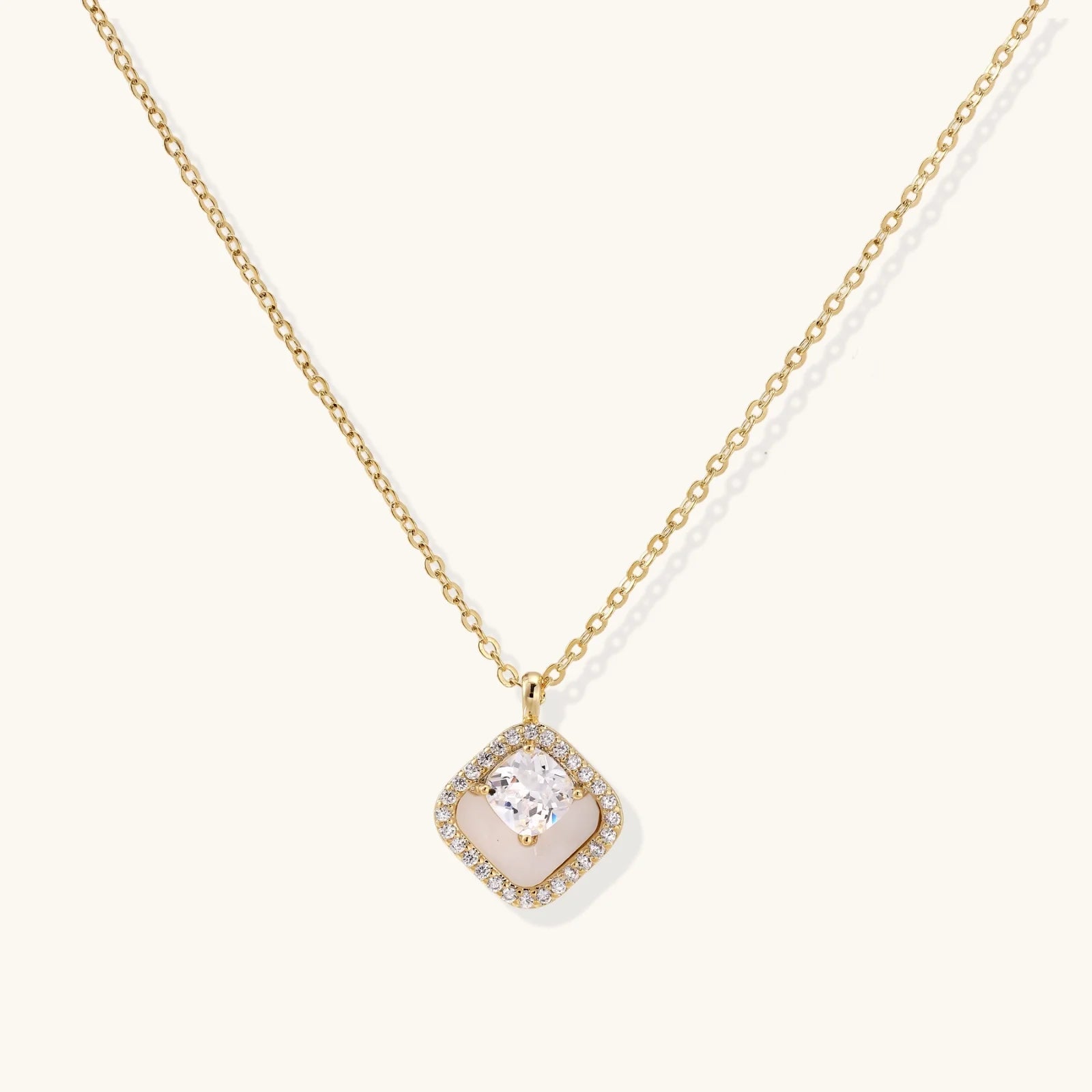Gold quatrefoil pendant with crystal center on iridescent mother-of-pearl base, adjustable gold chain on cream background