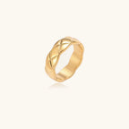 Close-up of an 18K gold-plated twisted band ring with dimensional braided pattern on cream background.