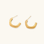 Gold-toned hoop earrings with hammered dimpled texture and post closure on cream background