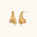 Pair of sculptural gold stud earrings with twisted organic forms on cream background