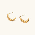 Gold-plated sculptural hoop earrings with chunky segmented design on cream background