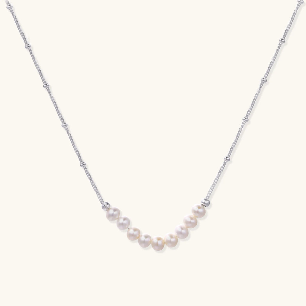 Delicate sterling silver chain necklace with small freshwater pearls arranged in a curved smile arc on cream background.