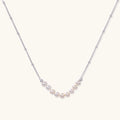 Delicate sterling silver chain necklace with small freshwater pearls arranged in a curved smile arc on cream background.