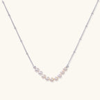 Delicate sterling silver chain necklace with small freshwater pearls arranged in a curved smile arc on cream background.