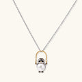 Whimsical owl pendant holding a white pearl on a gold swing, rhodium-plated silver chain on cream background.