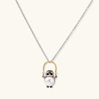 Whimsical owl pendant holding a white pearl on a gold swing, rhodium-plated silver chain on cream background.
