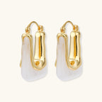 Sculptural gold-plated hoop earrings with flowing curved design and lever-back closure on cream background.