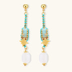 Gold-plated dangle earrings with turquoise threading, star charms, and white pearl beads against cream background.