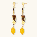 Gold-plated dangle earrings with brown gemstones, star charms, and yellow amber drops on cream background.