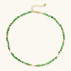 Layered necklace with green stone beads, gold spacers, white accents, and protective eye pendant on cream background.