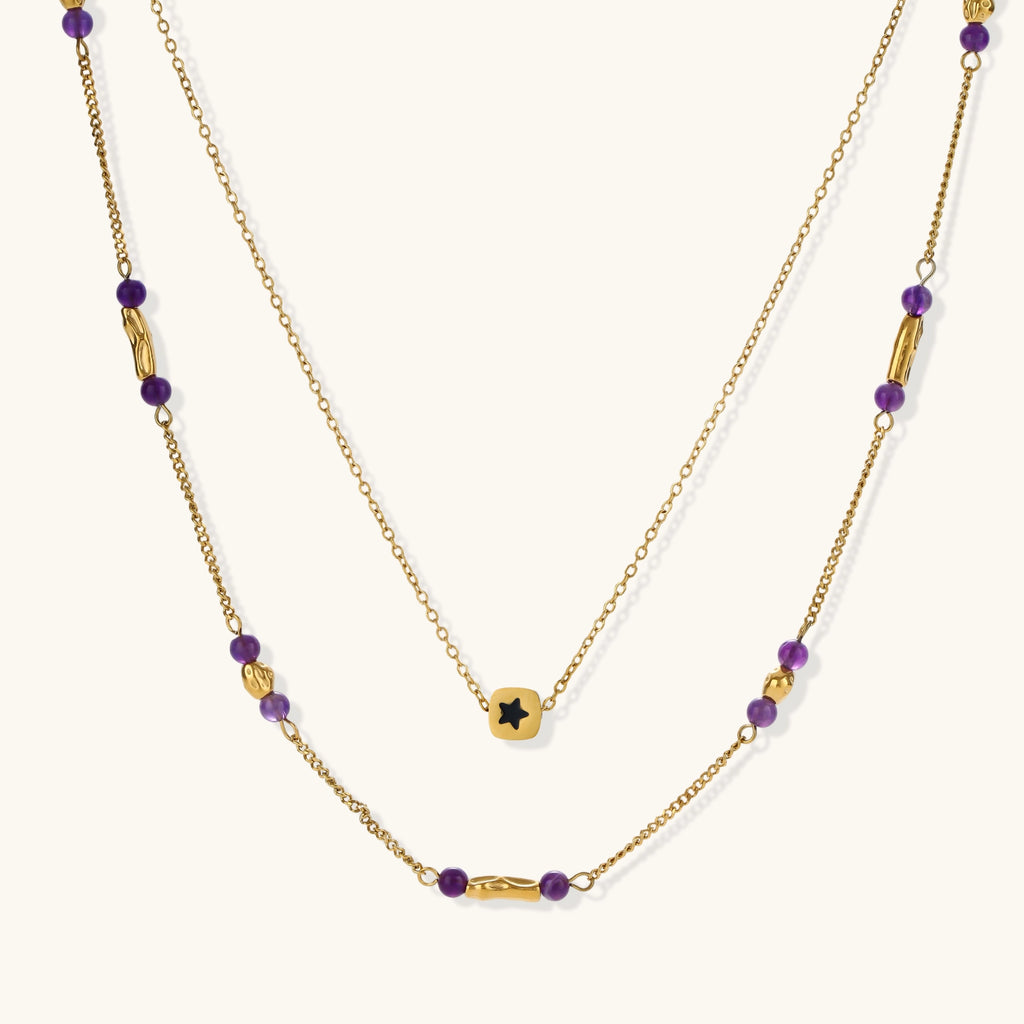 Two layered gold-tone necklaces with purple stone beads and star pendant against cream background.