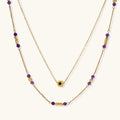 Two layered gold-tone necklaces with purple stone beads and star pendant against cream background.
