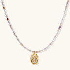 Delicate gold-plated necklace with mixed gemstone beads and ornate oval pendant on white background
