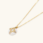 Gold-plated necklace with circular white enamel pendant featuring central zirconia stone and ornate decorative details