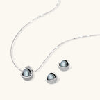 Elegant spherical pendant necklace and earrings set featuring crystal-pavé bottom half in gold or silver finish on white background.