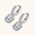 Sterling silver huggie hoops with emerald-cut moissanite drops featuring pavé-set crystals on white background.