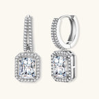 Sterling silver huggie hoops with emerald-cut moissanite drops featuring pavé-set crystals on white background.