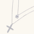 Two delicate sterling silver necklaces with moissanite stones - one solitaire pendant and one cross pendant on white background.